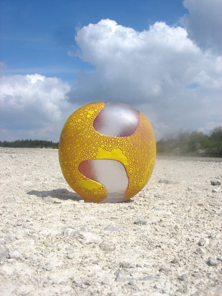 Sphère de verre jaune et blanche posée sur le sable, face au ciel.